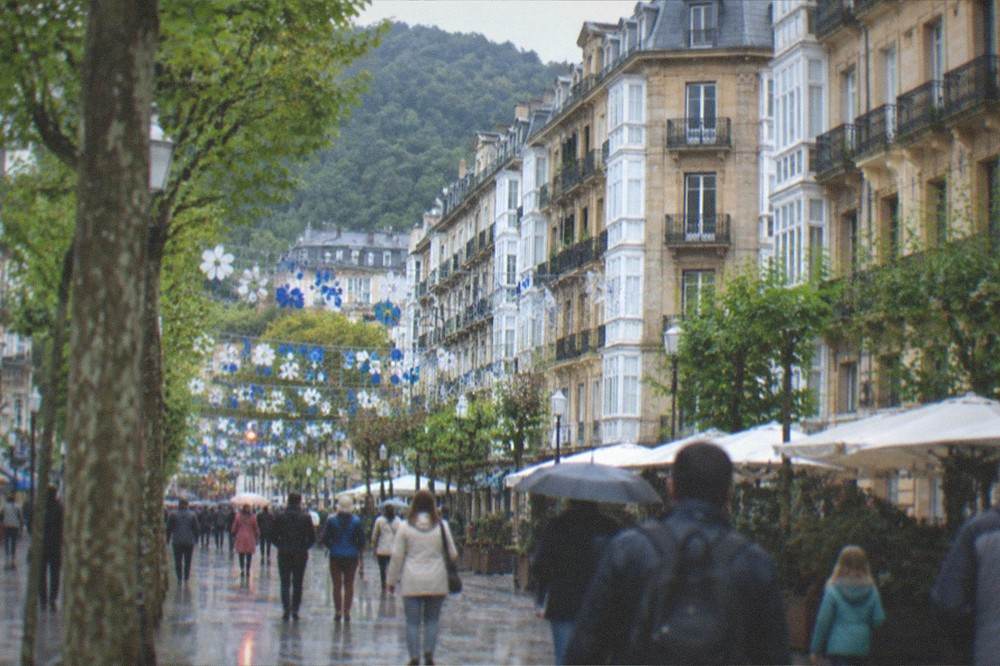 Families and visitors walking a decorated festival street in central San Sebastián in daylight