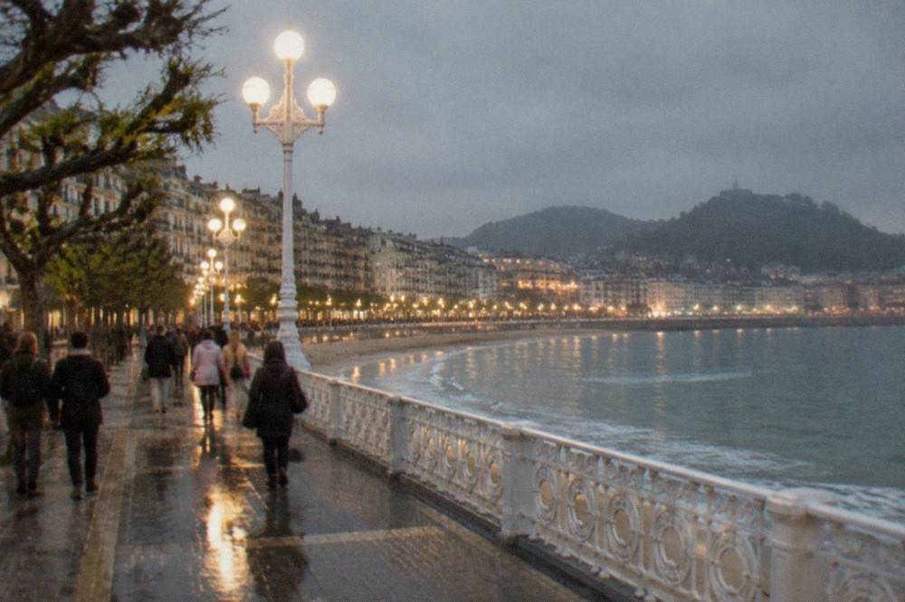 Festival crowds walking along the illuminated seafront promenade of La Concha bay at night