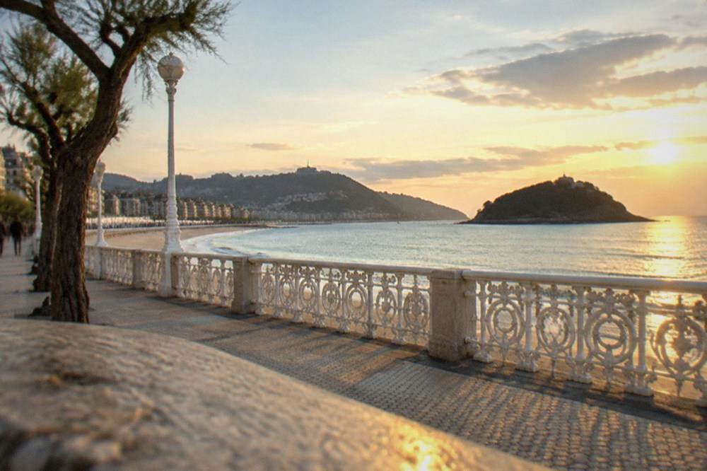 The curved railing of La Concha promenade with white railings and the island in the bay beyond