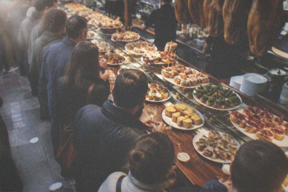 A busy pintxo bar in the Old Town of San Sebastián with crowds standing at the counter in the evening