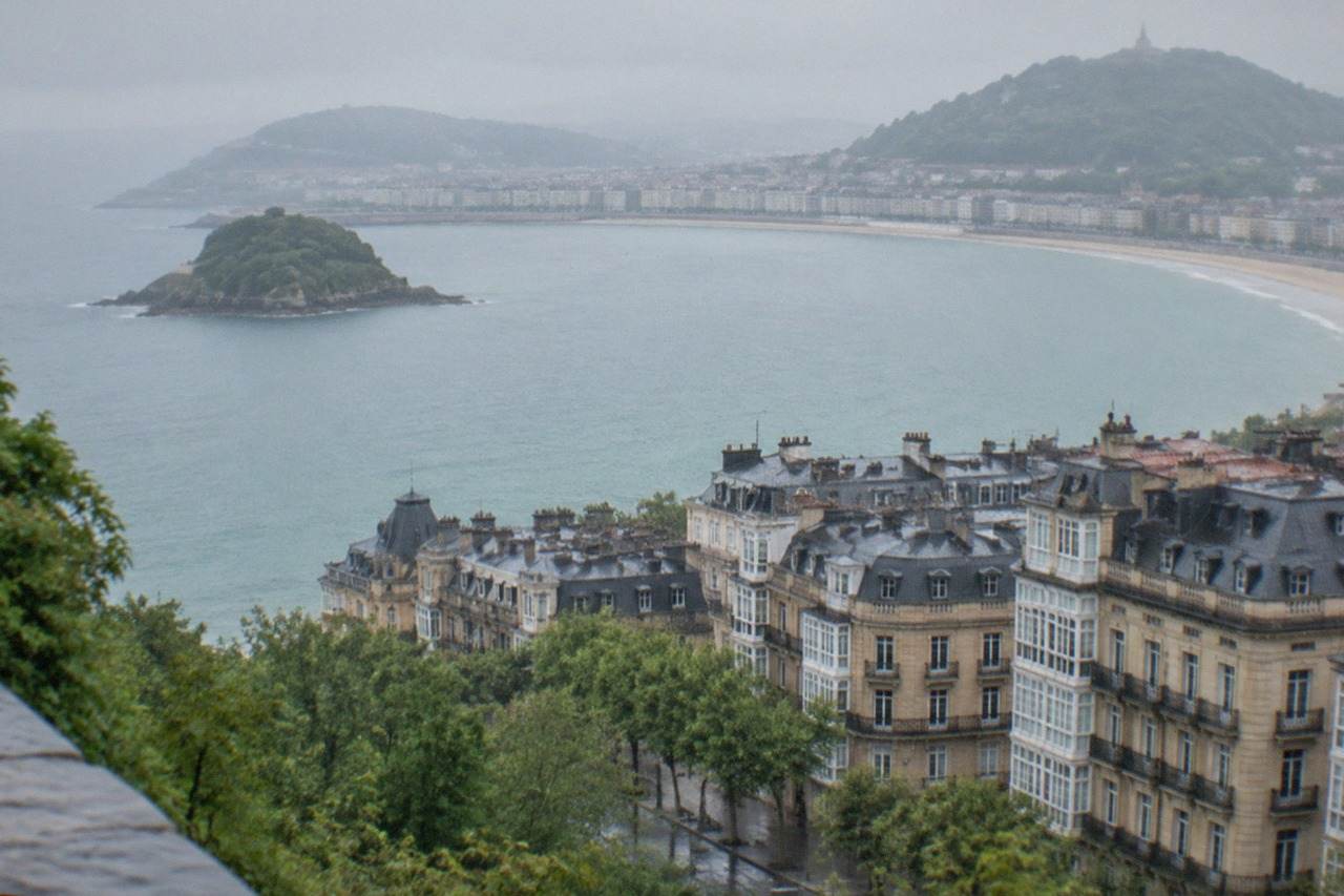 The curved bay of San Sebastián seen from a high hillside, with the island and the city's rooftops along the water