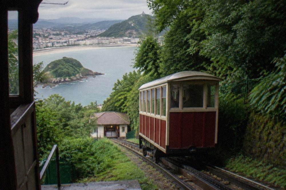A wooden funicular car on a steep rack railway climbing a wooded hill above a bay