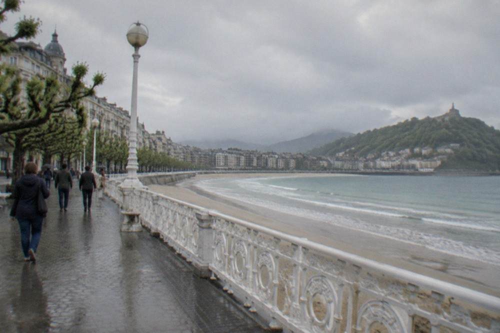 A wet seafront promenade along La Concha with grey clouds over the bay