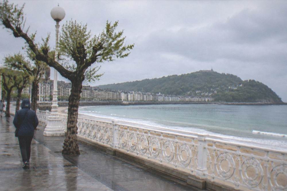A visitor in a rain jacket walking the seafront promenade beside La Concha bay