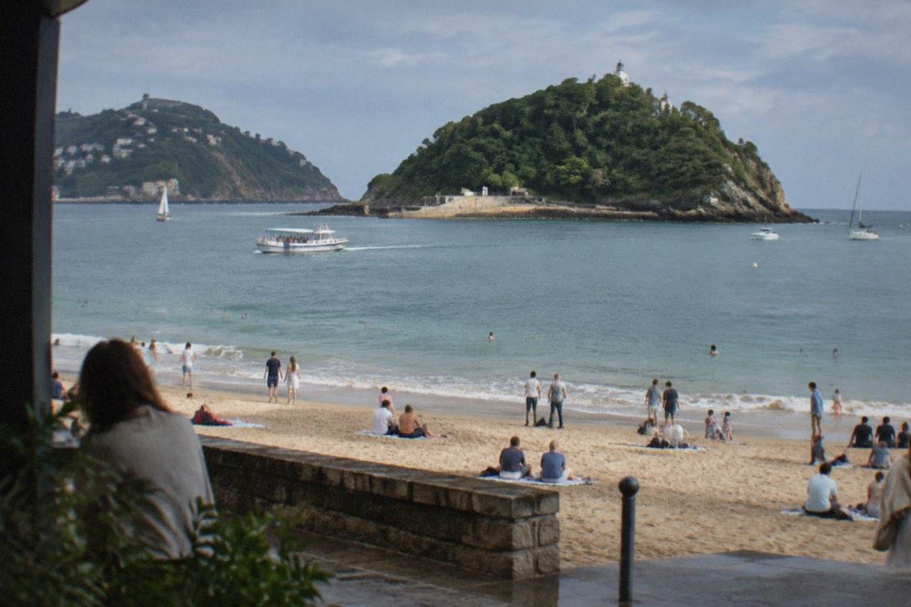 La Concha beach in San Sebastián on a busy summer day, with the bay and Santa Clara island behind
