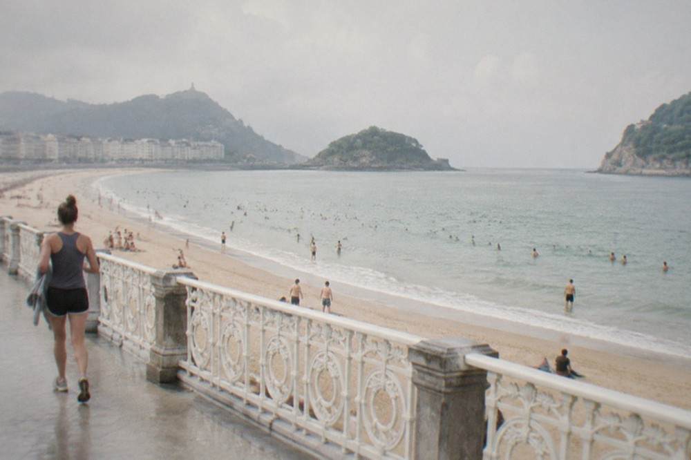 People swimming from La Concha beach in San Sebastián with white tents and the bay curve behind