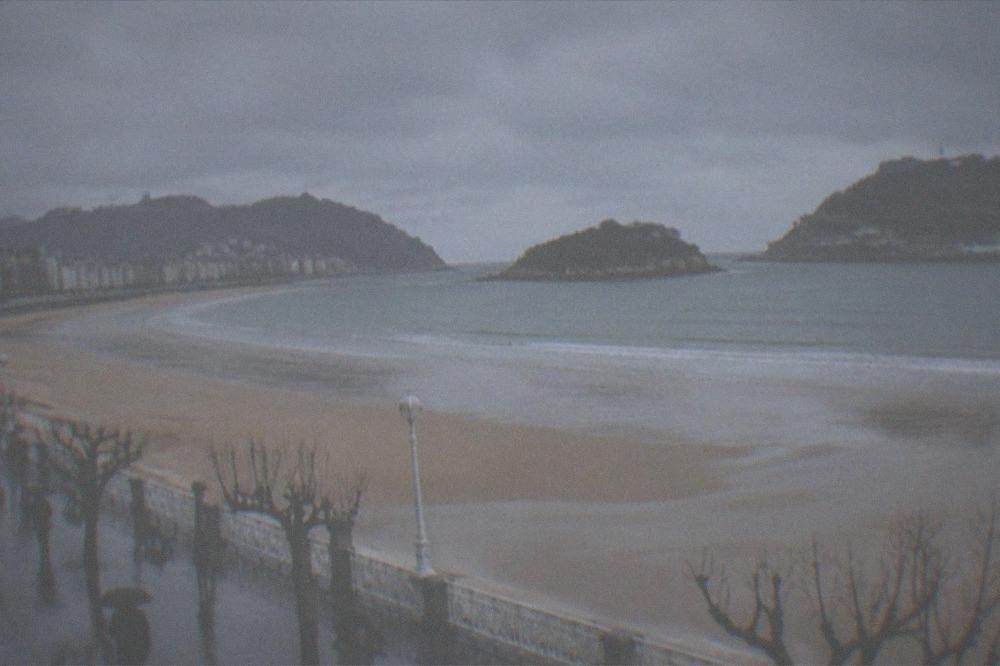 Empty wet sand at La Concha beach in winter with the bay and hills behind