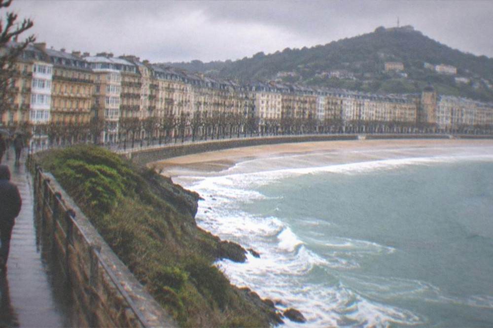 A walker in a rain jacket on the coastal path above the bay with breaking waves below