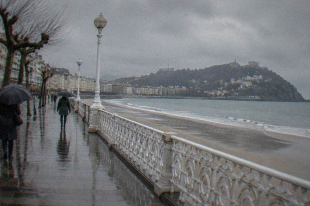 Rain clouds over La Concha beach with wet sand and an empty promenade in winter