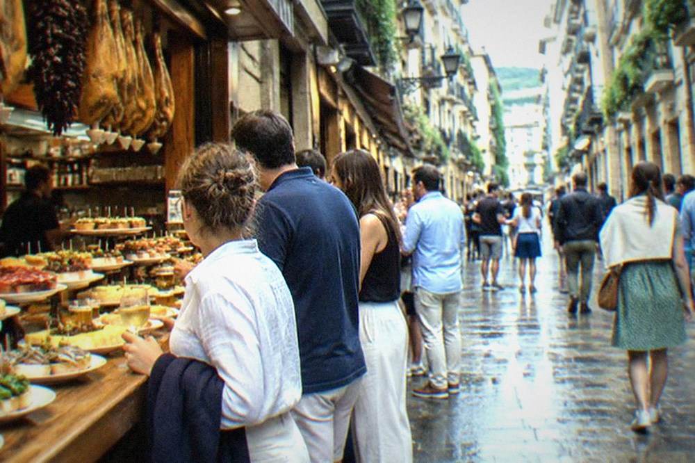 A narrow Old Town street in San Sebastián with pintxo bars and people outside on a warm evening