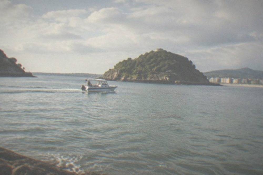 A small boat crossing La Concha bay toward Santa Clara island on a calm summer afternoon