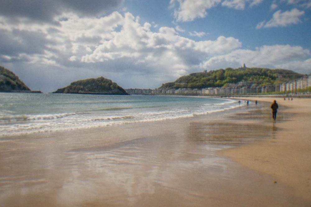 Clouds and sunshine over La Concha beach with wet sand and few people