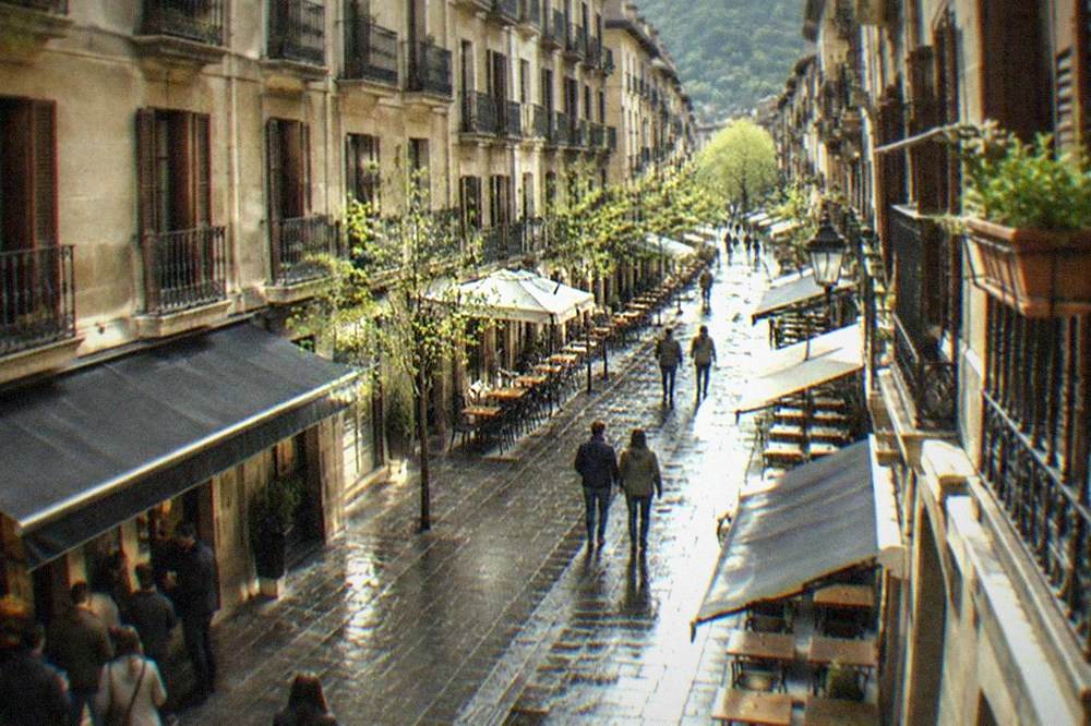 A quiet Old Town street in San Sebastián with bar awnings and empty tables in early spring