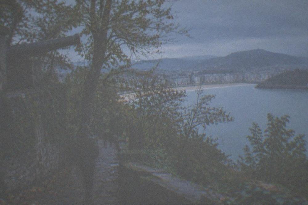 A walker in a rain jacket on the Monte Urgull path above San Sebastián with the bay below