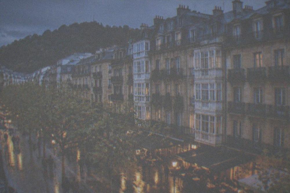 A rain-slicked street in the Old Town of San Sebastián with bar lights reflecting on the pavement