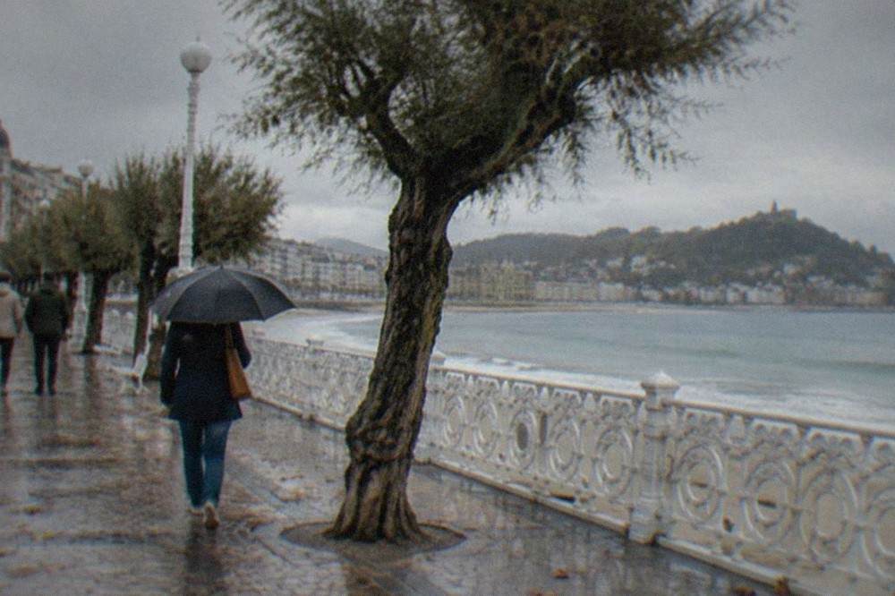 People walking along the La Concha promenade under white railings with the bay behind them
