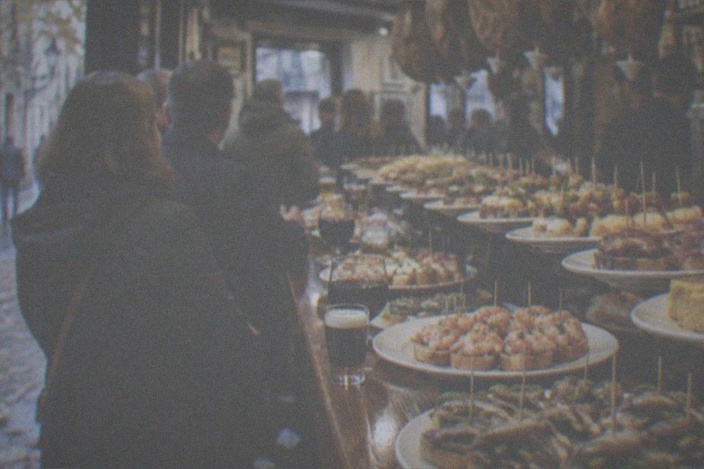 A crowded pintxo bar counter in the Old Town of San Sebastián with plates of small skewered snacks