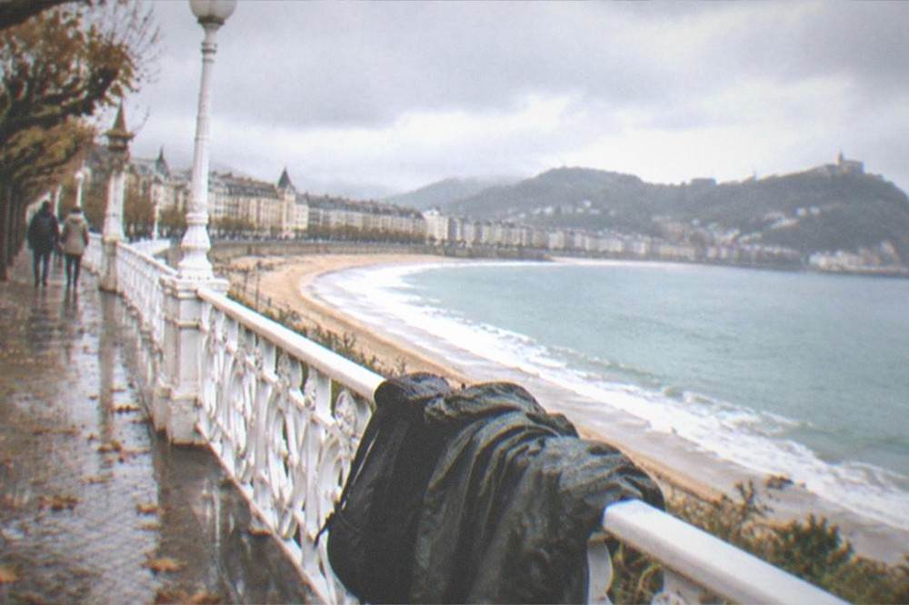 A rain jacket and backpack resting on a promenade railing overlooking the bay