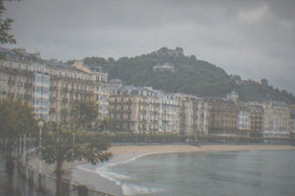Rain clouds gathering over a coastal city with a curved bay and green hills