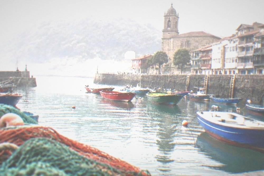A small coastal town with a stone church tower and fishing boats in a harbour