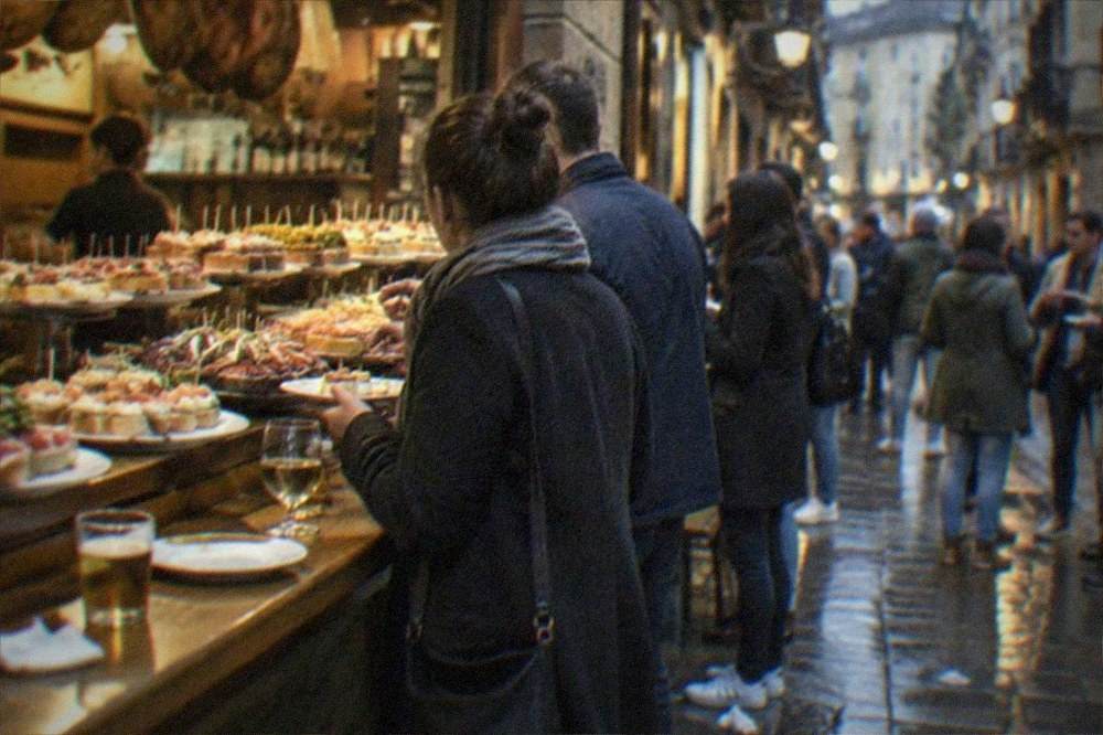 A narrow old town street at dusk with bar counters in doorways and people standing with small plates