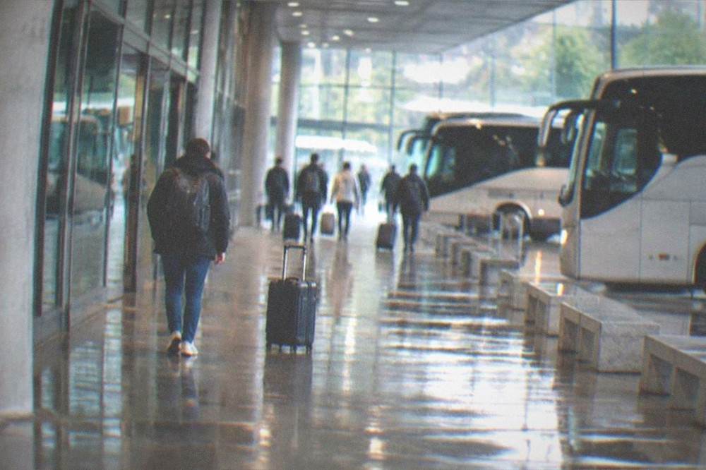 A traveller walking away from a station entrance with a backpack, leaving a wheeled suitcase behind