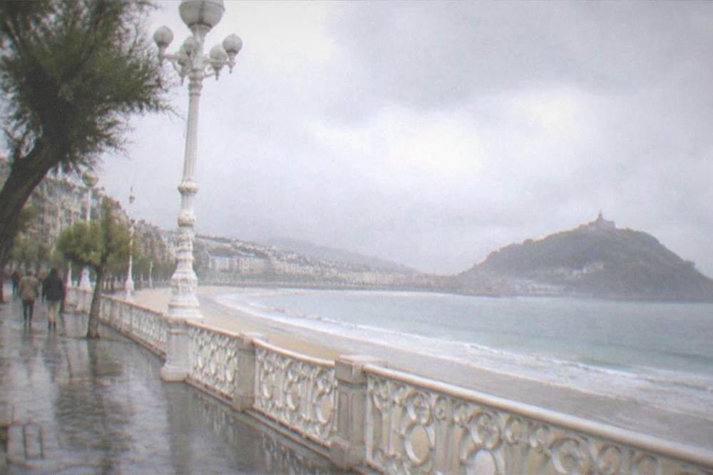 Rain clouds over La Concha bay with wet promenade and the island beyond