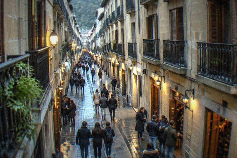 People walking through a lit narrow Old Town street in San Sebastián in the evening