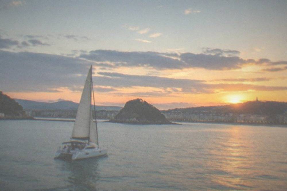 Catamaran sailing on La Concha bay at sunset with the city lights behind