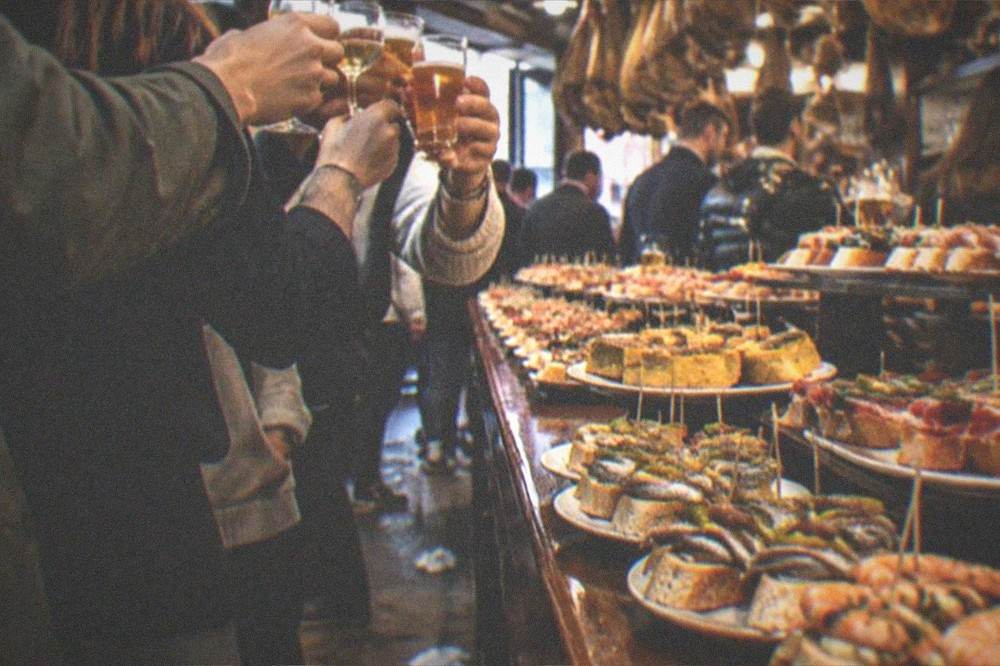 Group of friends toasting with small glasses at a crowded bar counter at night