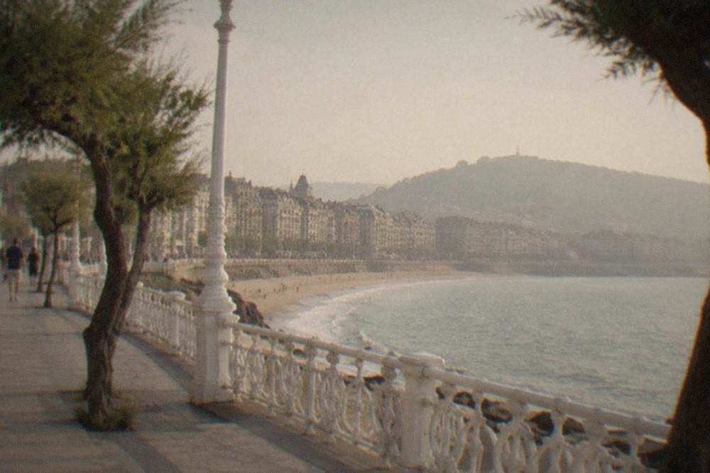 The curved railing and promenade of La Concha beach at golden hour with people walking