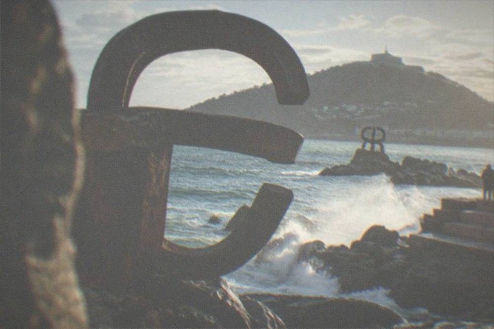 The three steel sculptures of the Peine del Viento standing on wet rocks with waves breaking around them