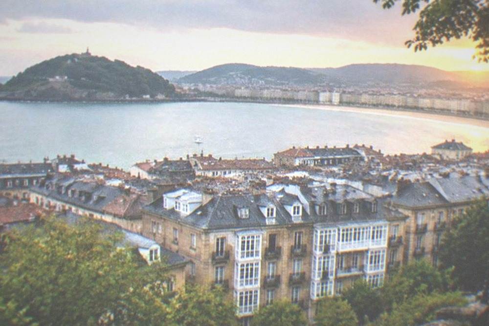 Old Town rooftops of San Sebastián seen from a Monte Urgull path at sunset with the bay beyond