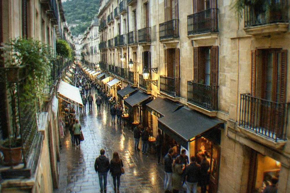 A narrow old town street lined with small shops and bar awnings in the evening