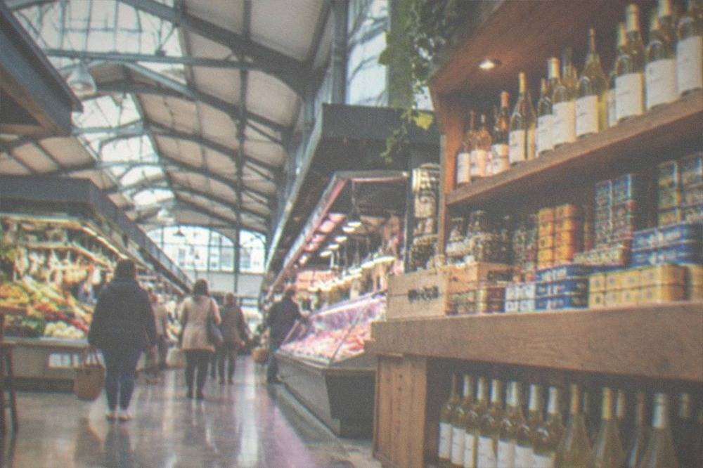 A shop counter displaying bottles of white wine, cider and tinned foods on wooden shelves
