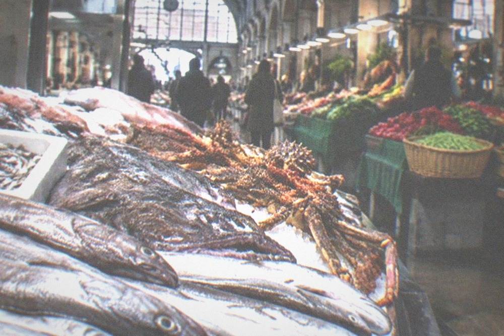 A market hall interior with stalls of produce, fish and cheese under a high ceiling