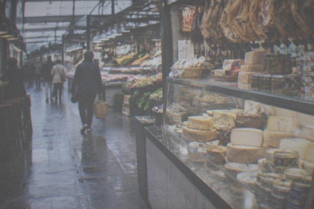 A small gourmet shop counter with cheese, ham and tinned goods displayed behind glass