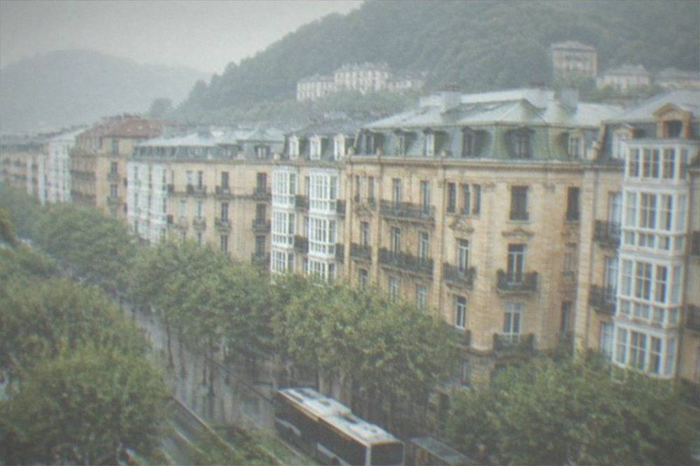 A city bus waiting at a stop on a tree-lined street in San Sebastián