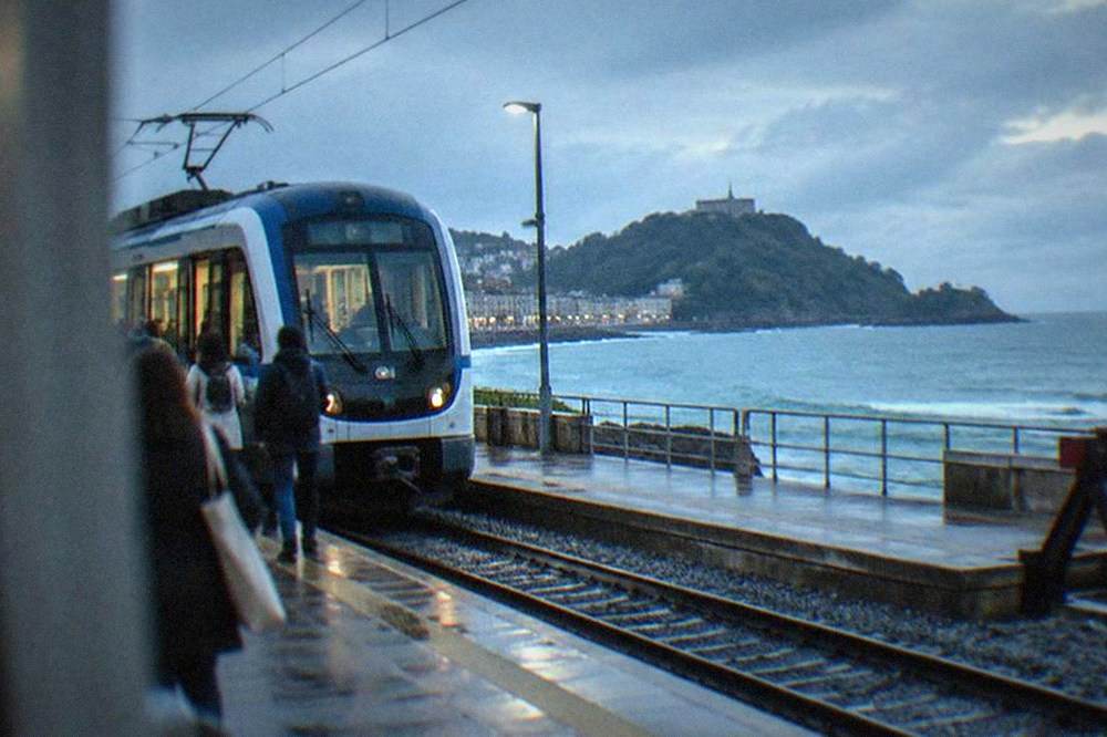 A narrow-gauge train at a coastal platform station in the Basque Country