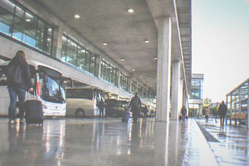 A regional bus at a sheltered stop outside a small airport terminal