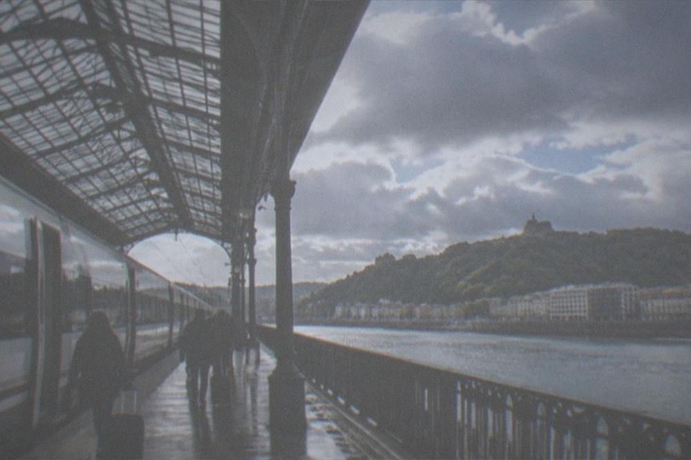A long-distance train at a station platform beside a river in San Sebastián