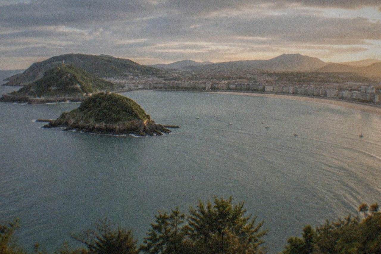 The curved sandy bay of La Concha in San Sebastián seen from above, with the island and green hills behind the water