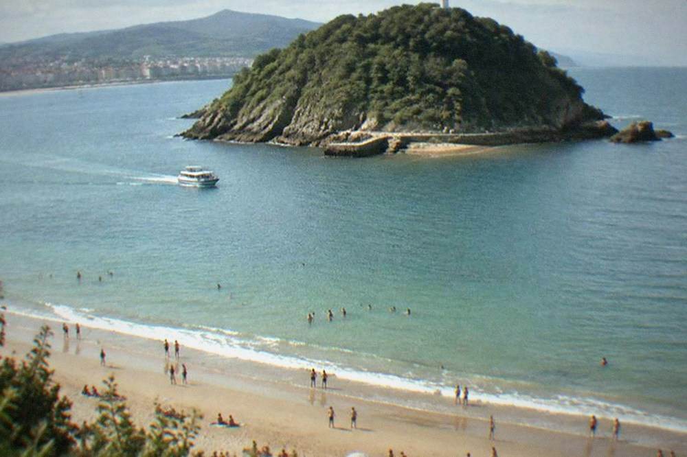 Swimmers and sunbathers on the sand of La Concha beach with the island of Santa Clara offshore