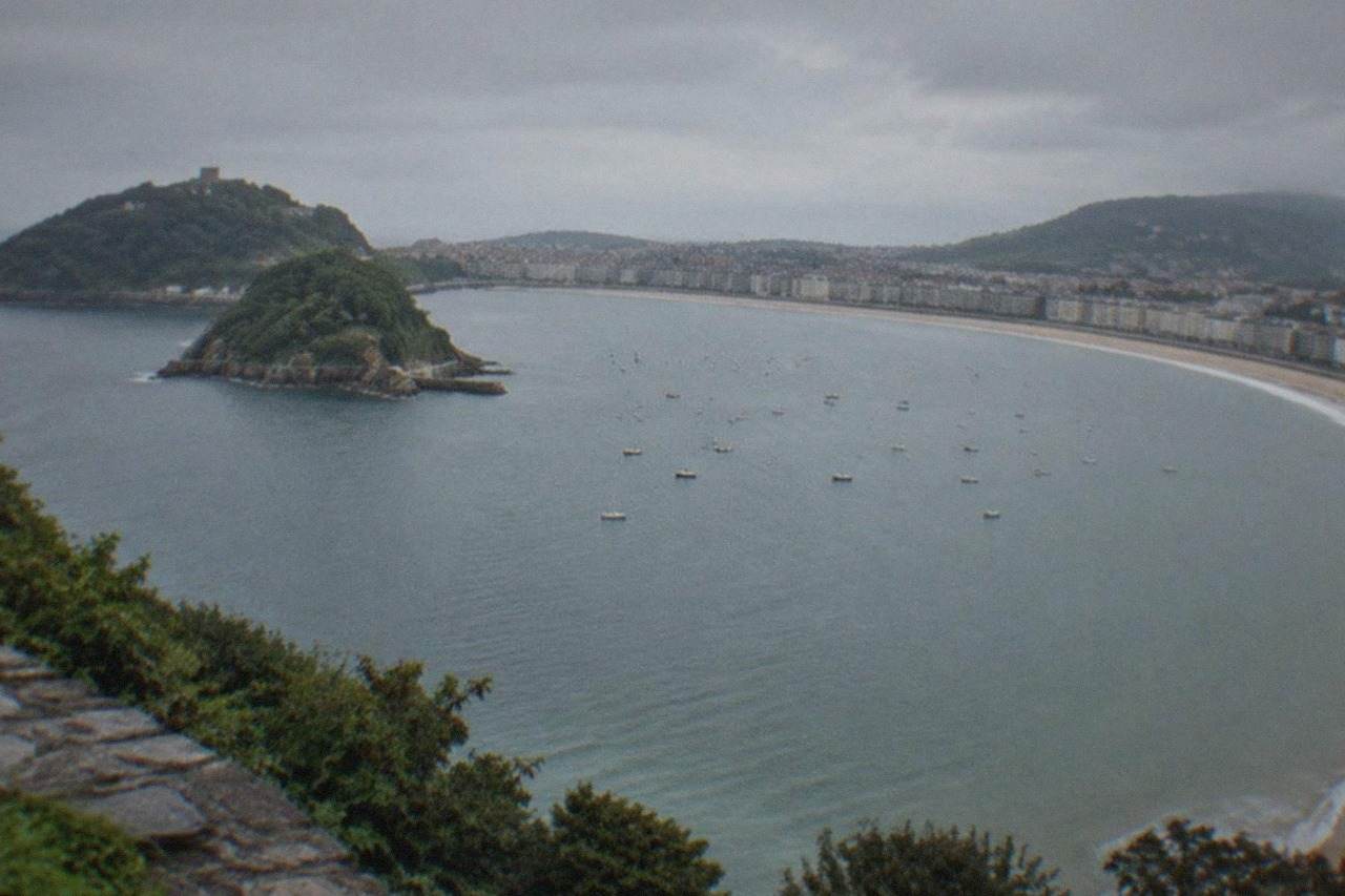 The curved sandy bay of La Concha in San Sebastián seen from above, with the island and green hills behind