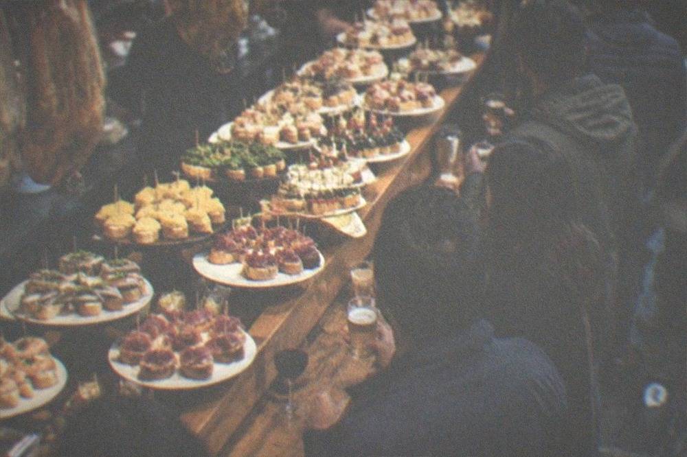 A crowded pintxo bar counter in the old town with plates of small skewered bites laid out