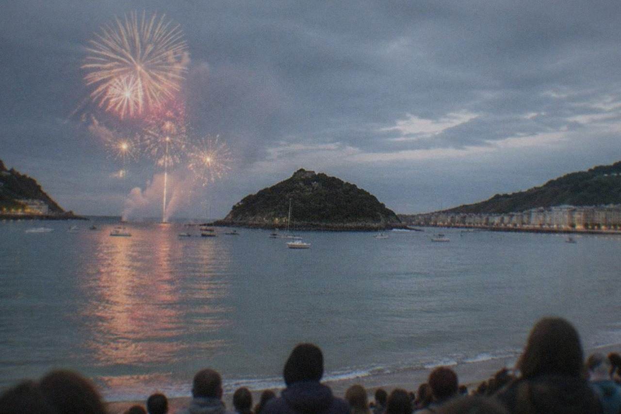 Crowds gathered along La Concha bay in San Sebastián at dusk with fireworks bursting over the water