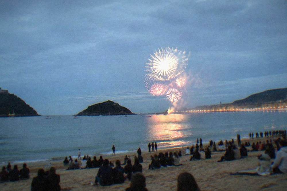 People watching a fireworks display from the sand of La Concha beach at night