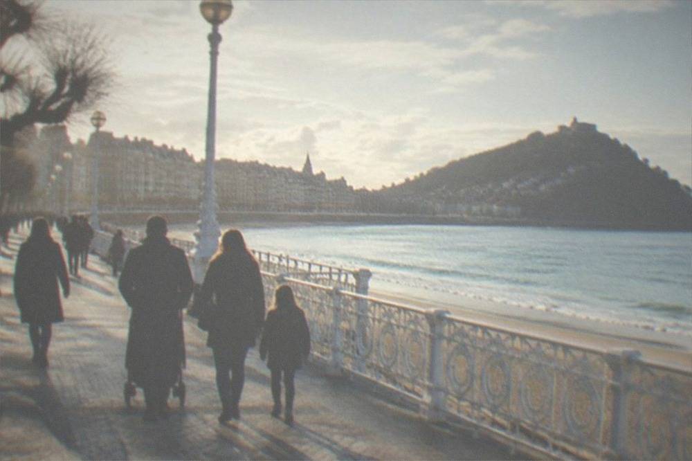 Families walking along the illuminated seafront promenade of San Sebastián during a festival evening