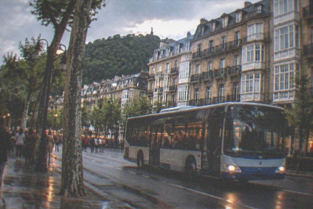 A city bus moving along a street in central San Sebastián in the evening with festival crowds on the pavement