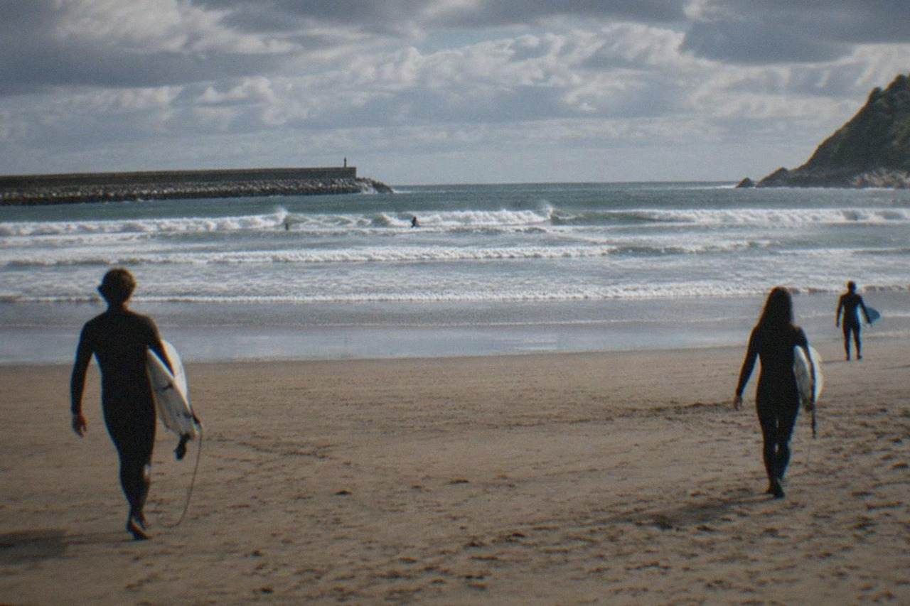 Surfers walking across the wide sandy Zurriola beach in San Sebastián with boards under their arms